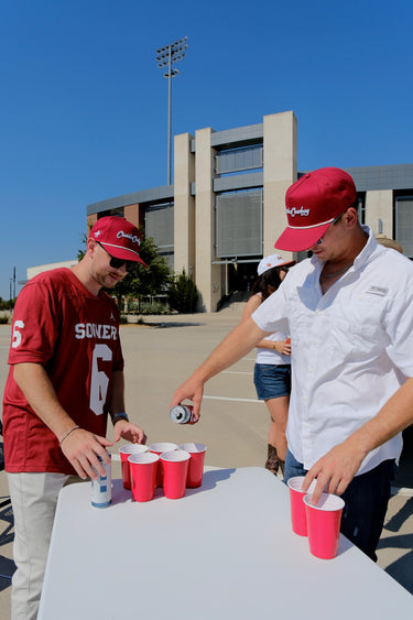 Friends at a tailgate wearing Classic Cowboy Norman crimson roper snapbacks.