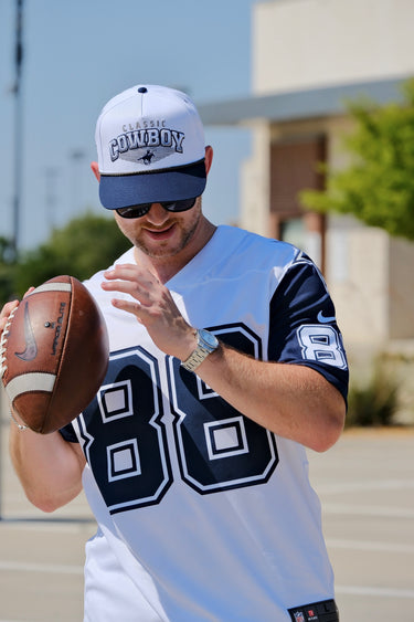 Man wearing the Classic Cowboy Trinity white and navy roper snapback while holding a football.