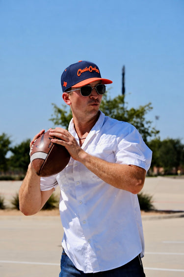 Man wearing the Classic Cowboy Wildcatter navy and coral snapback while throwing a football.