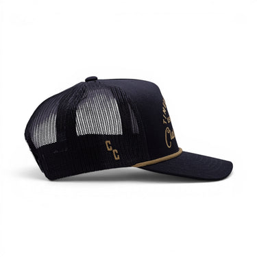 The Outpost all-black trucker hat with breathable mesh back, side view.