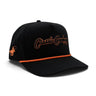 Classic Cowboy The Boone black roper snapback with orange rope and orange script embroidery, angled view.